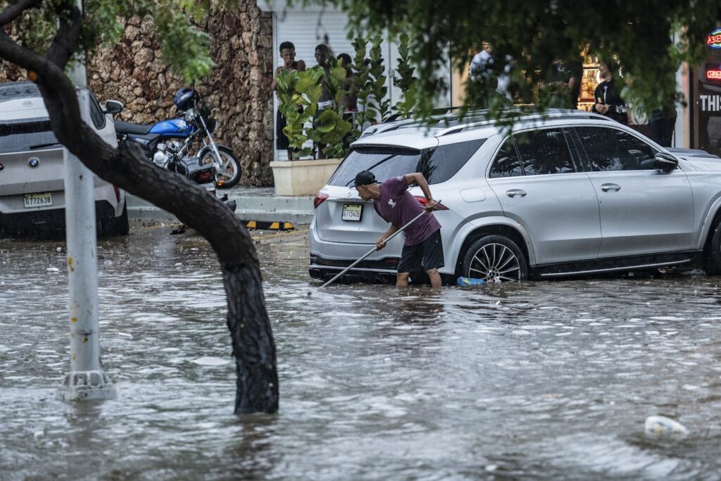 Rue innondé avec ujn homme qui retire l'eau autour d'une voiture