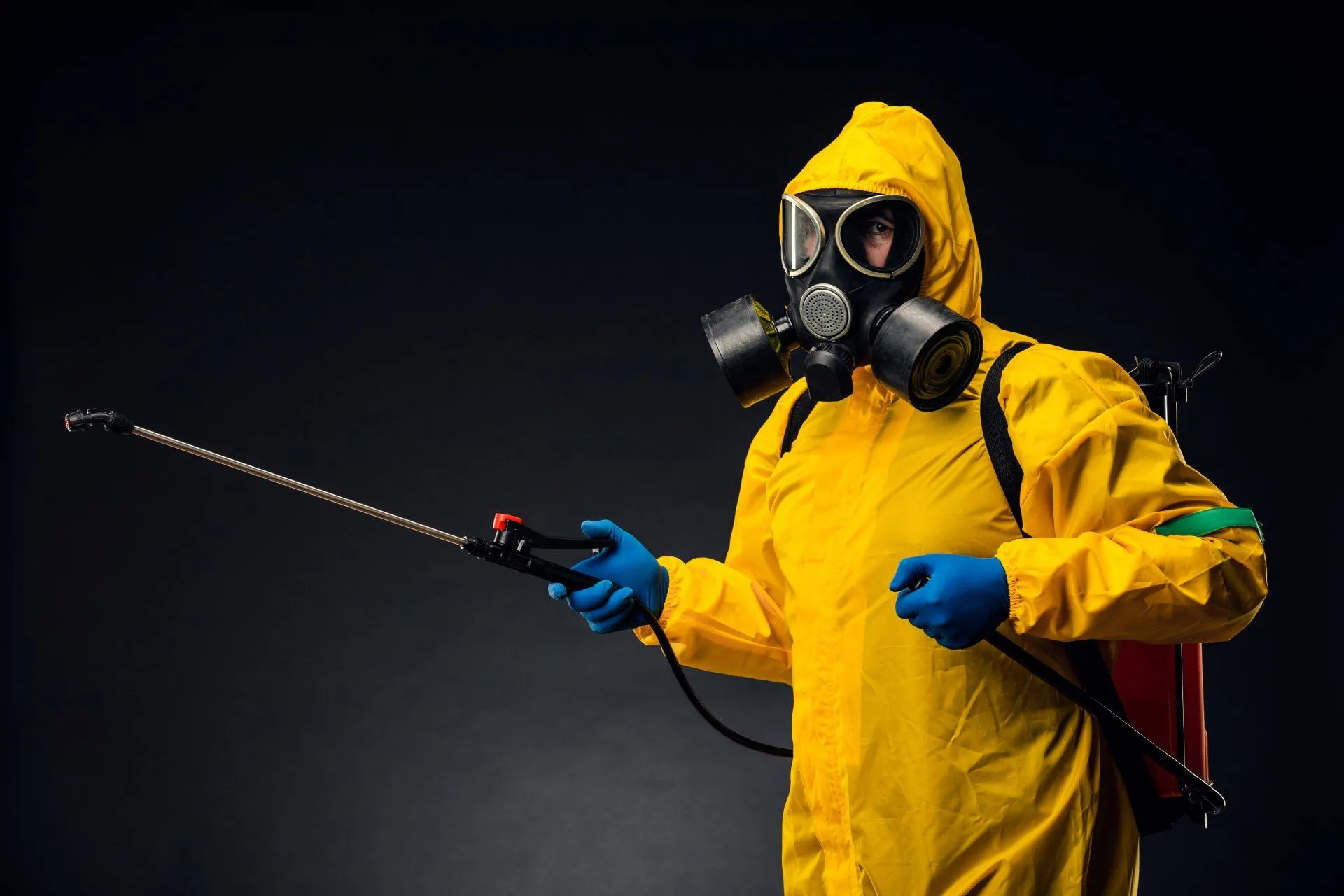 Homme avec un masque et une combinaison jaune qui désinfecte avec un pulvérisateur