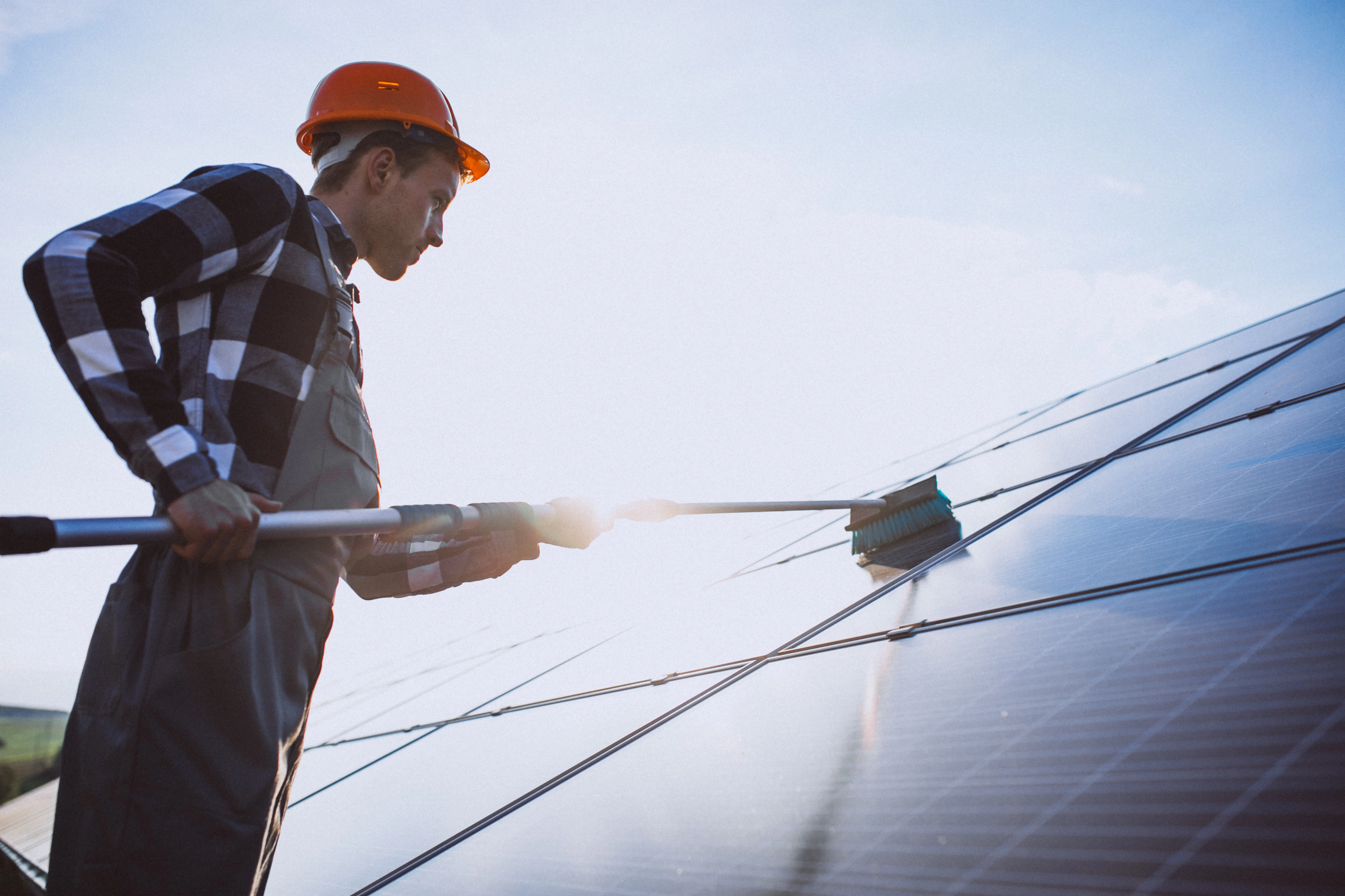 Homme qui nettoie des panneaux solaires avec une perche et une brosse